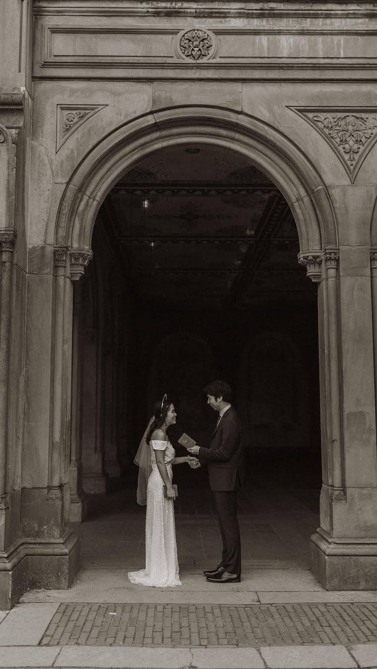 Bride and groom exchanging vows under a grand stone archway in sepia tones.