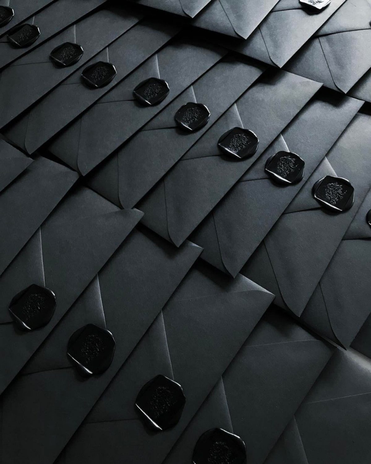Matte black envelopes with black wax seals arranged in overlapping rows.