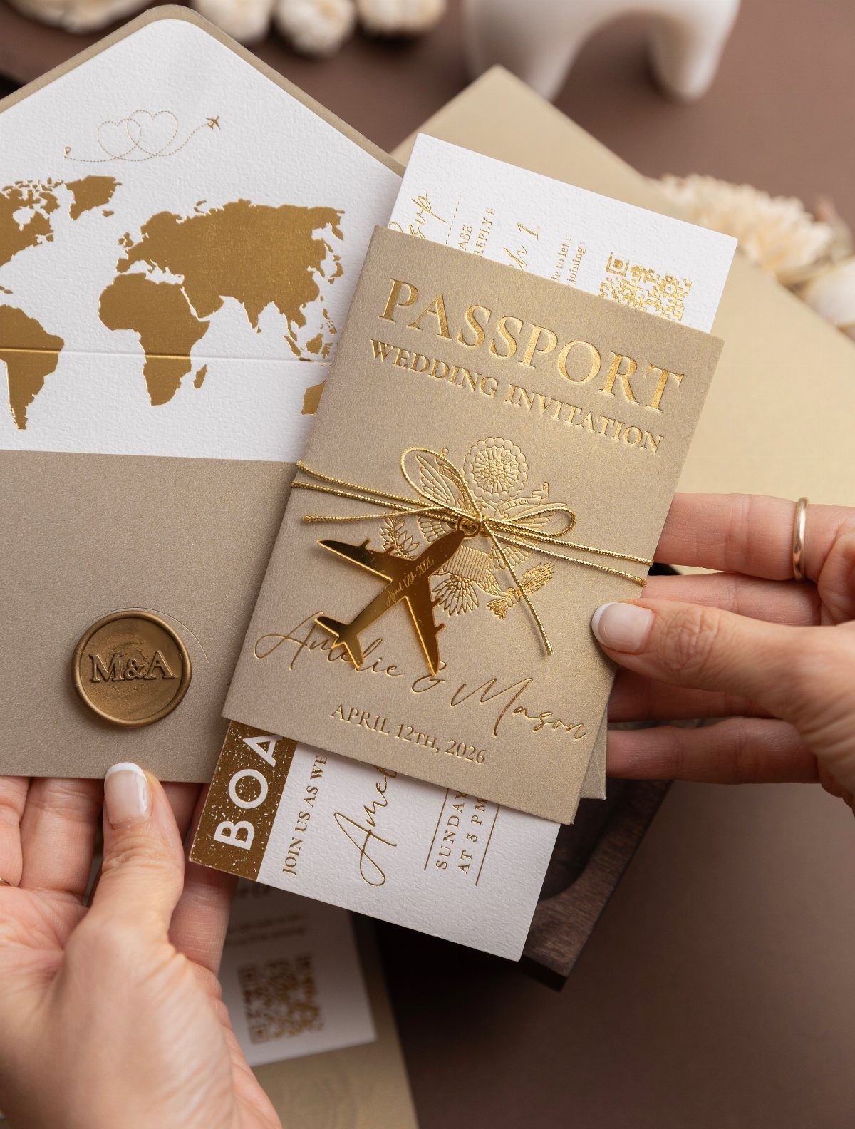 Passport-style wedding invitation with gold airplane charm and world map envelope liner.