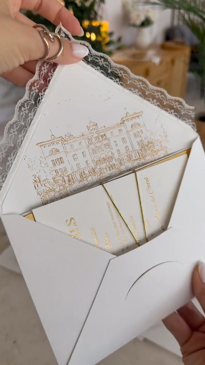 White wedding invitation envelope with gold foil building illustration and lace trim.