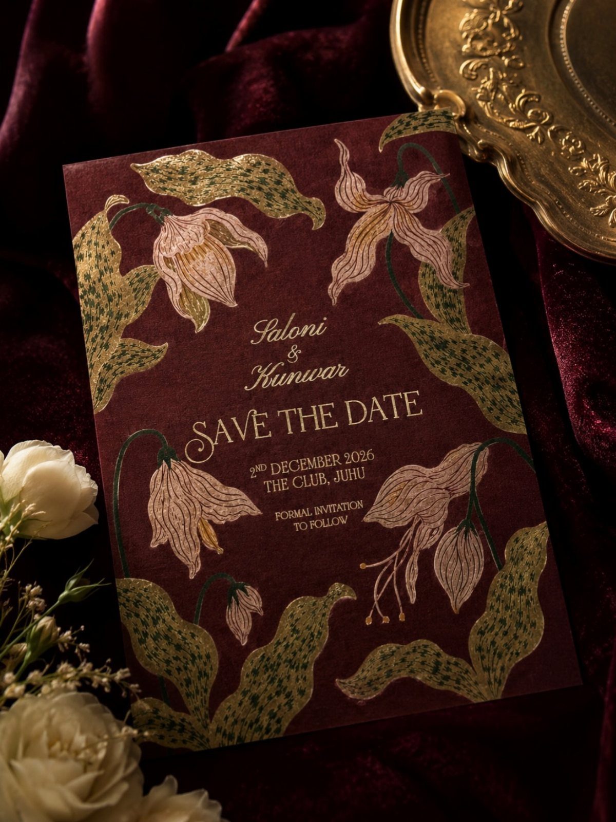 Burgundy save the date card with gold floral illustrations on red velvet fabric.