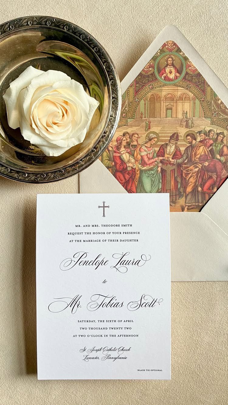 Wedding invitation with calligraphy and a religious painting envelope next to a white rose.