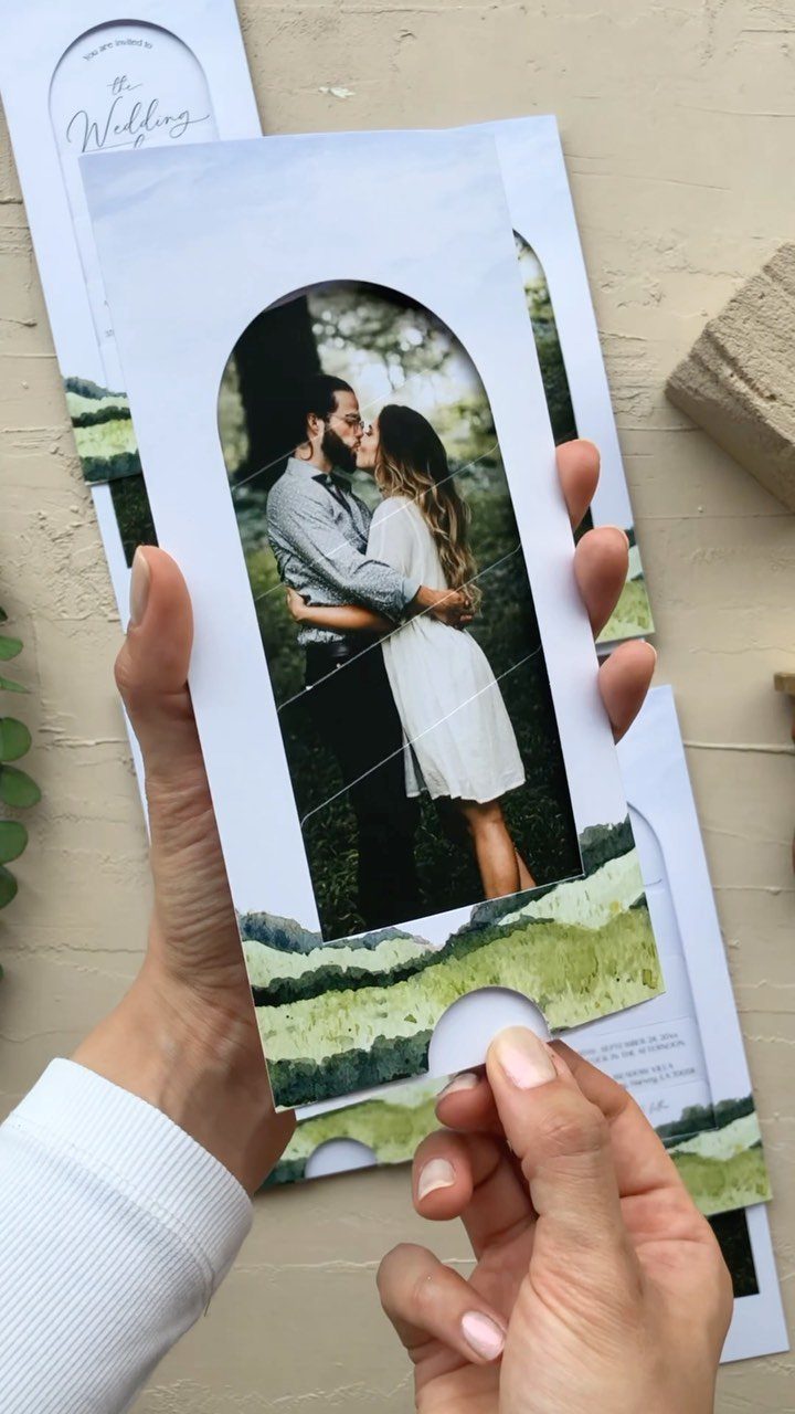 Wedding invitation with an arched photo of a couple kissing and green landscape.