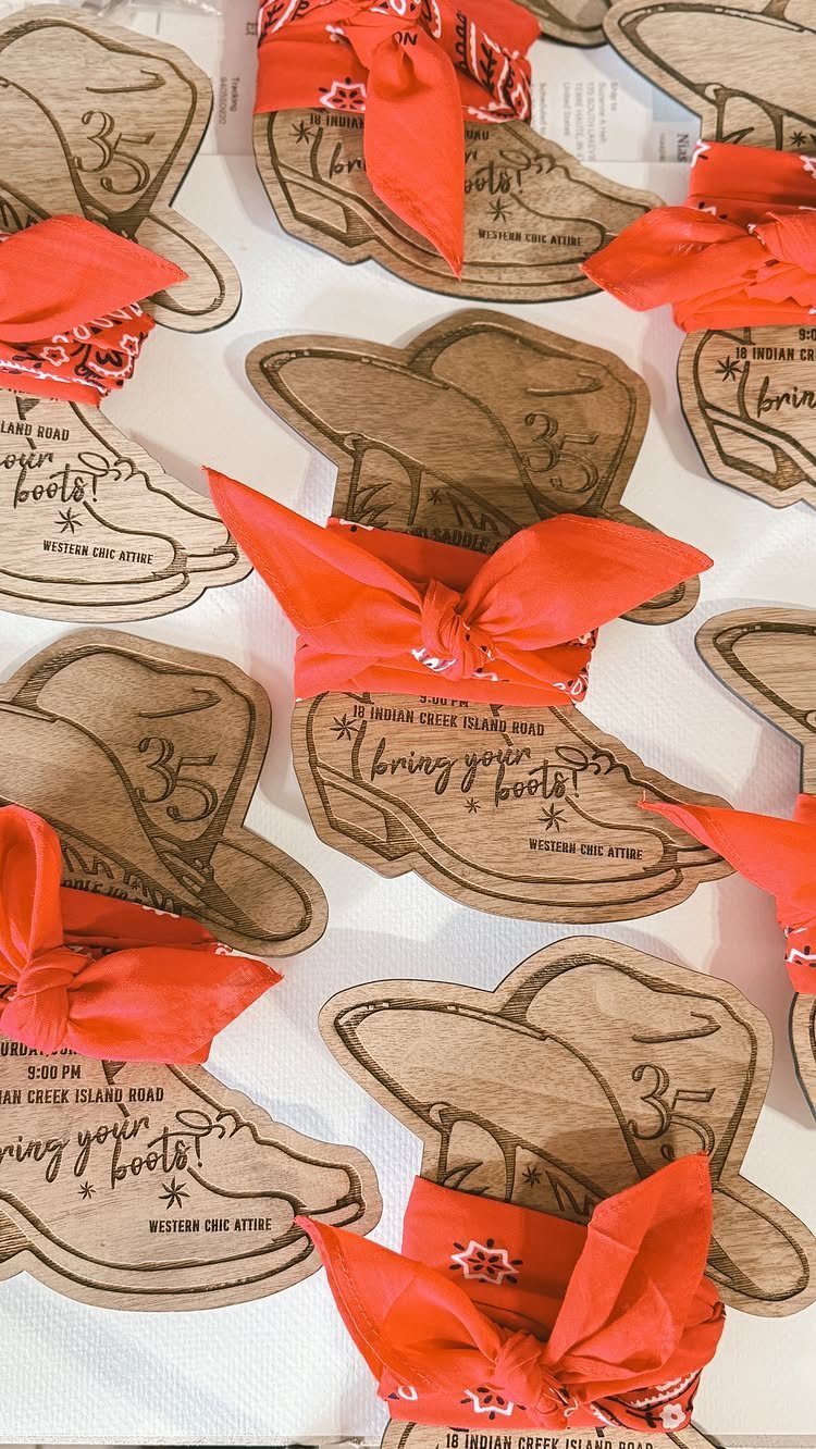 Wooden wedding invitations shaped like cowboy boots and hats tied with red bandanas.