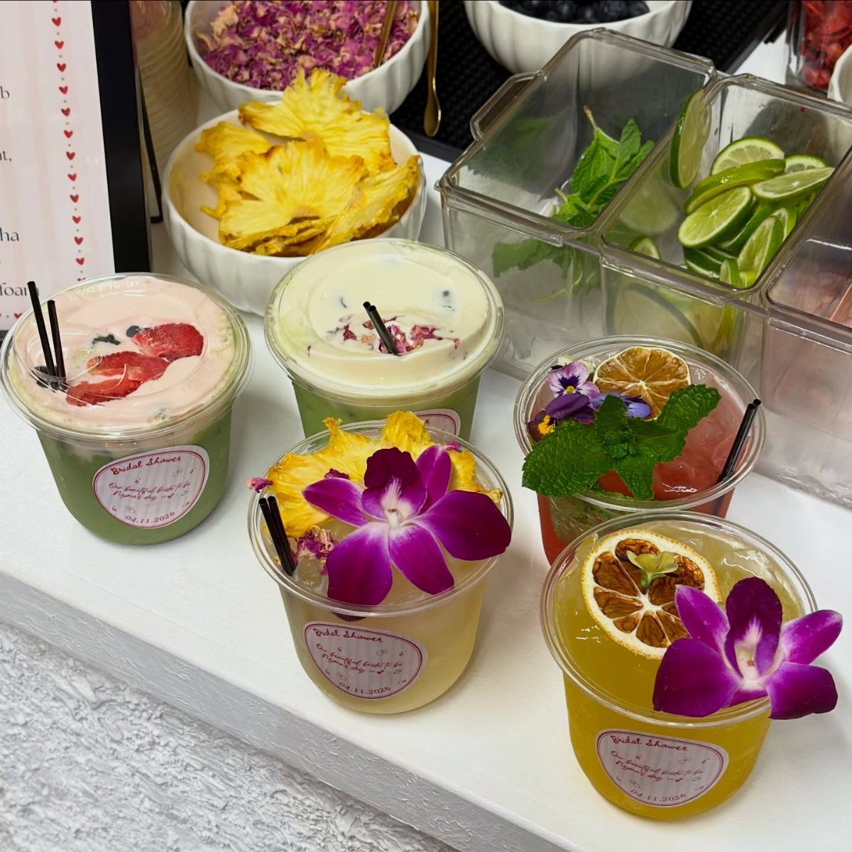 Colorful layered drinks topped with edible flowers and citrus slices on a white table