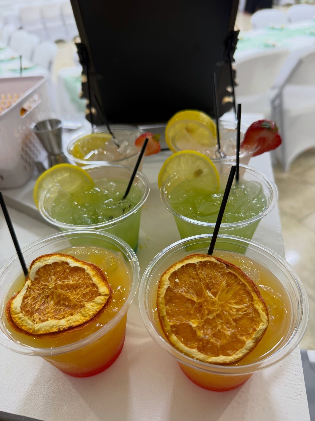 Colorful cocktails in plastic cups with citrus garnishes on a white table.