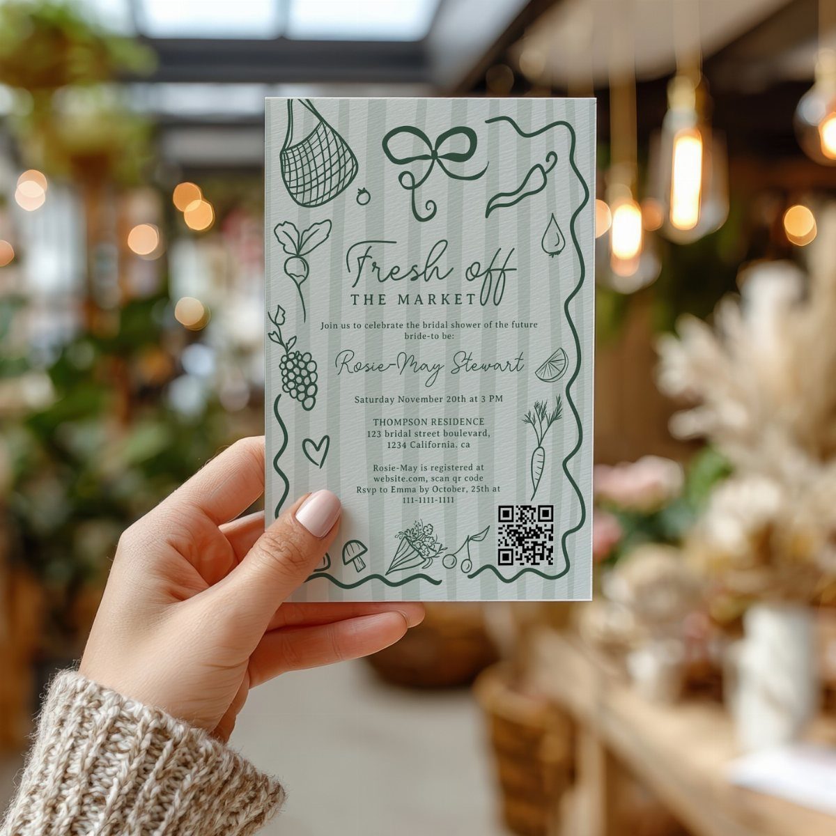 Hand holding a green and white market themed bridal shower invitation card.