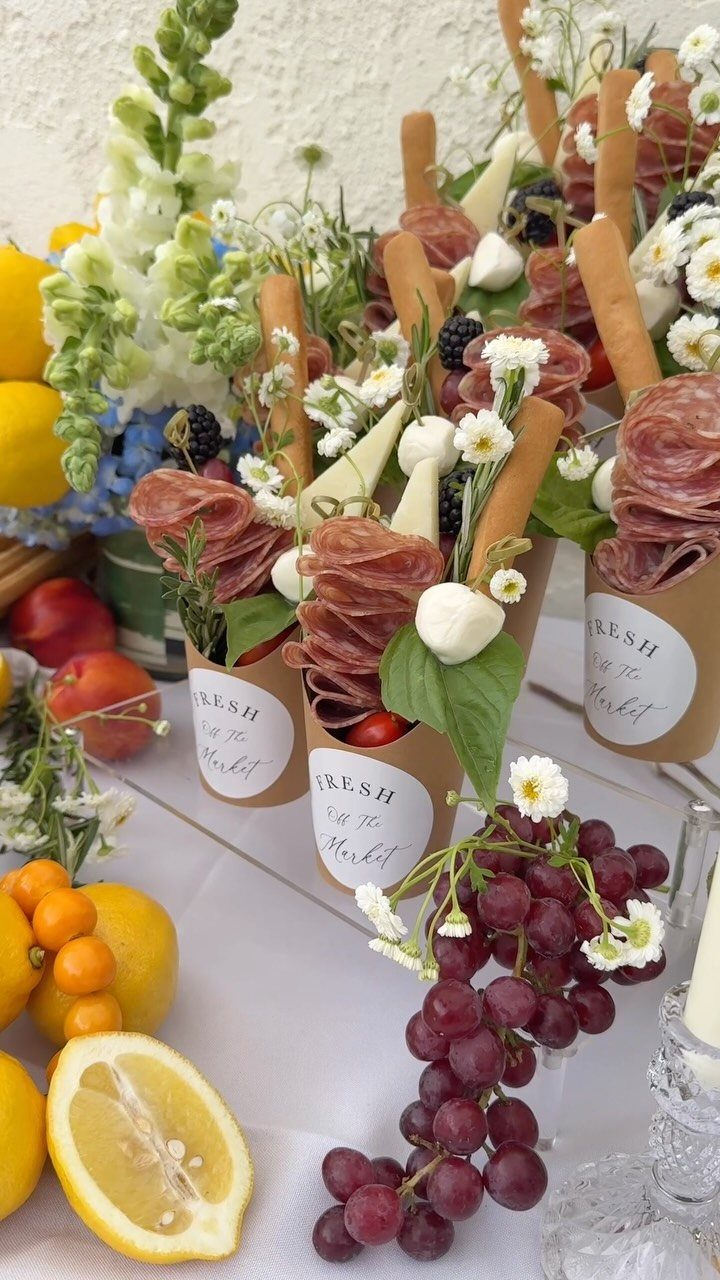 Charcuterie cones with meats and cheeses arranged on a table with fresh fruit.