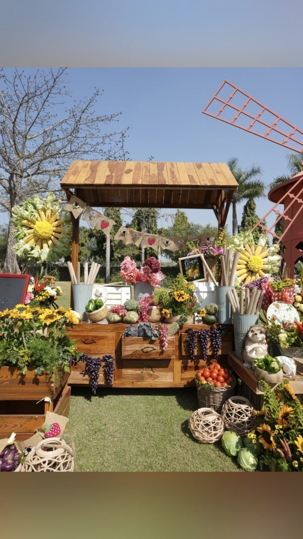 Wooden market stall decorated with fresh produce, sunflowers, and bunting on green grass.