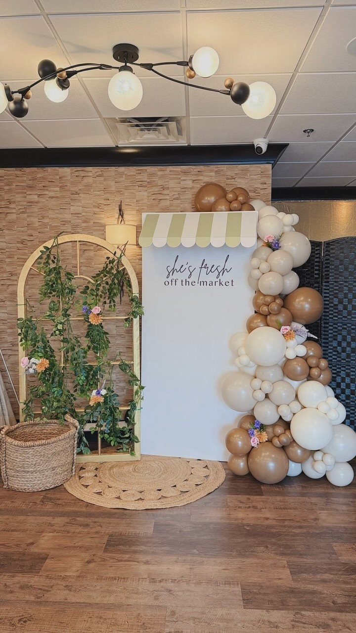 Bridal shower backdrop with market awning, balloon arch, and greenery trellis.