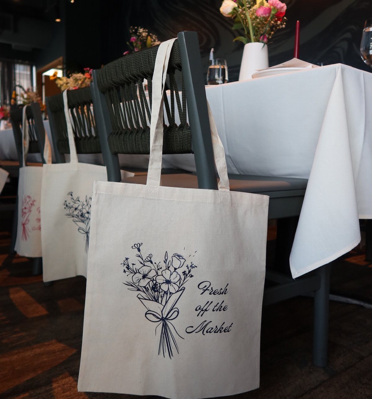 Canvas tote bags with floral illustrations and Fresh off the Market text hanging on chairs.