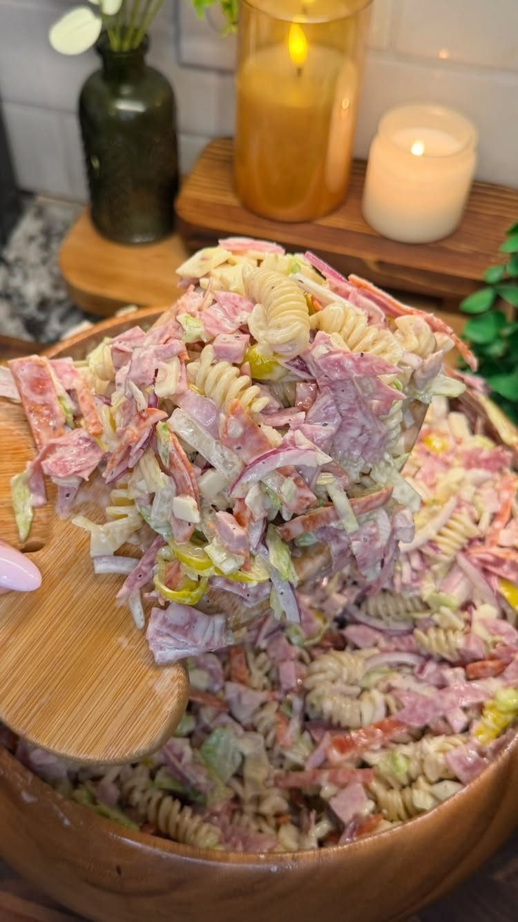 Pasta salad with rotini and ham being lifted by a wooden spoon.