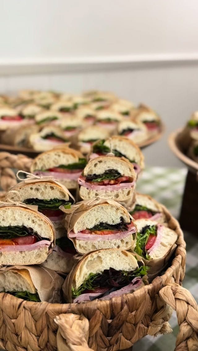 Small sandwiches wrapped in brown paper and string inside a woven wicker basket.