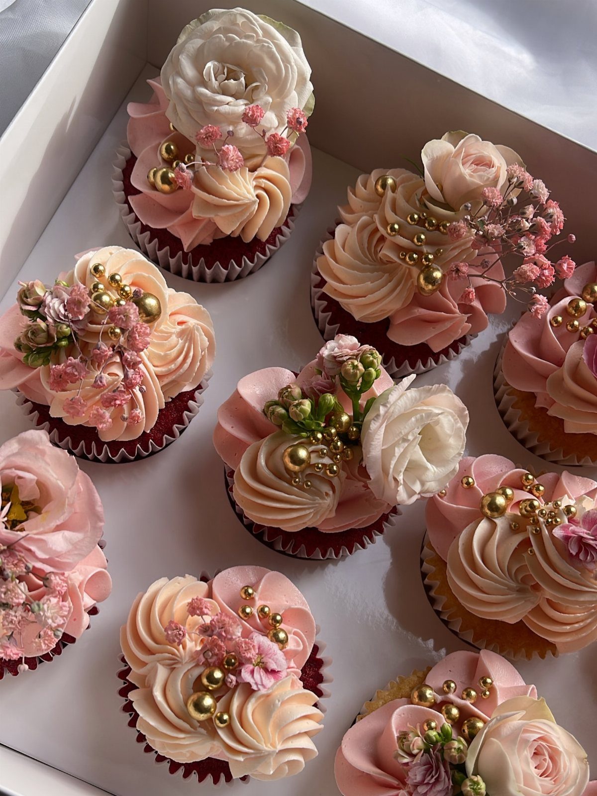 Cupcakes with peach frosting decorated with delicate pink and white edible flowers.