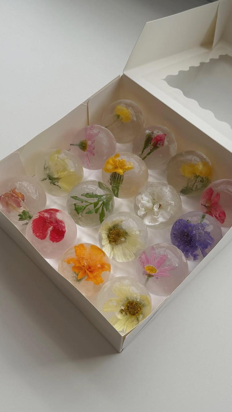Spherical ice balls with colorful wildflowers inside a white cardboard box.