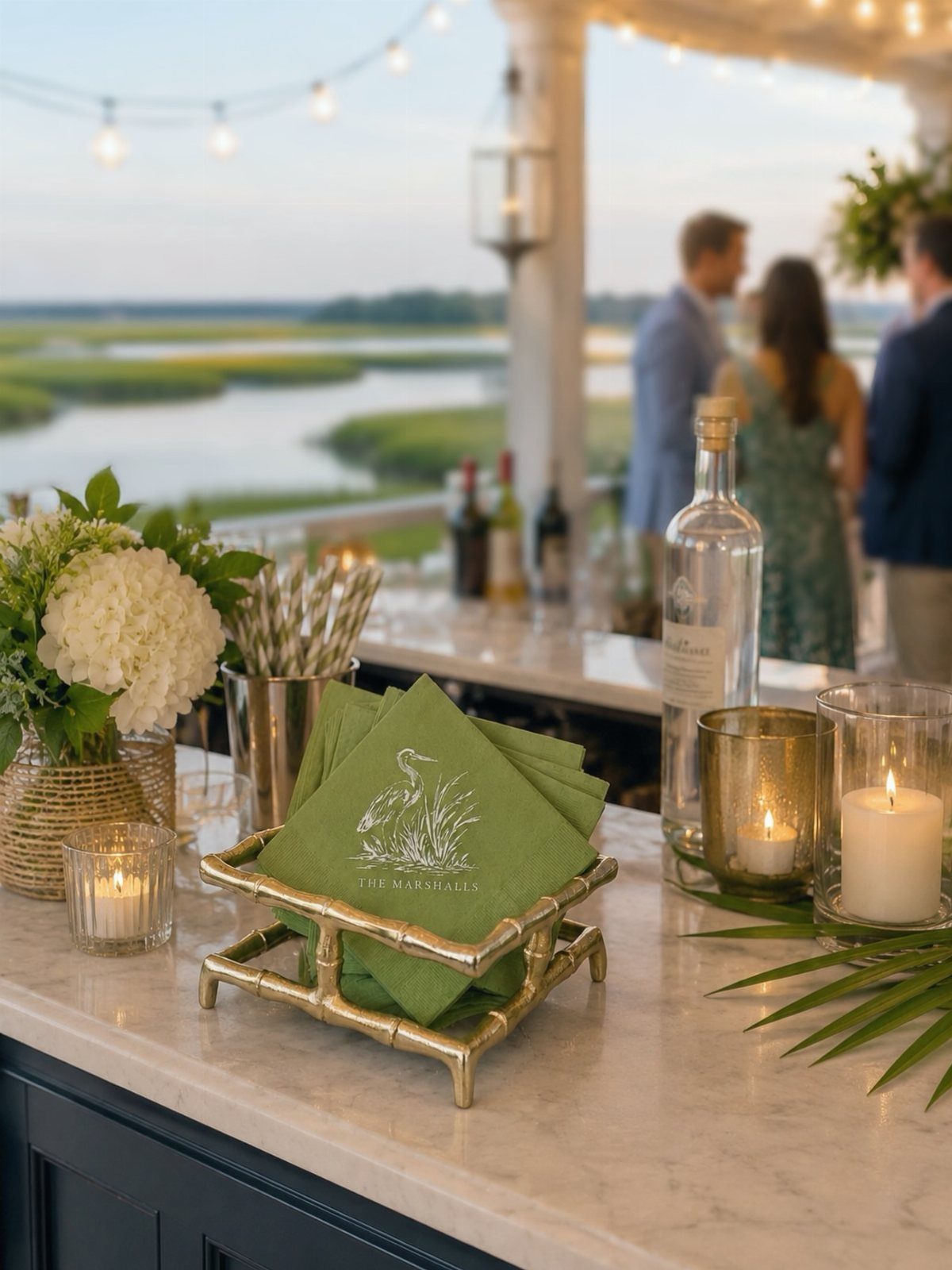 Green branded napkins in a gold holder on a marble bar with candles.