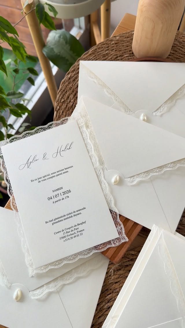 White wedding invitations with lace trim and pearl details on a woven mat.