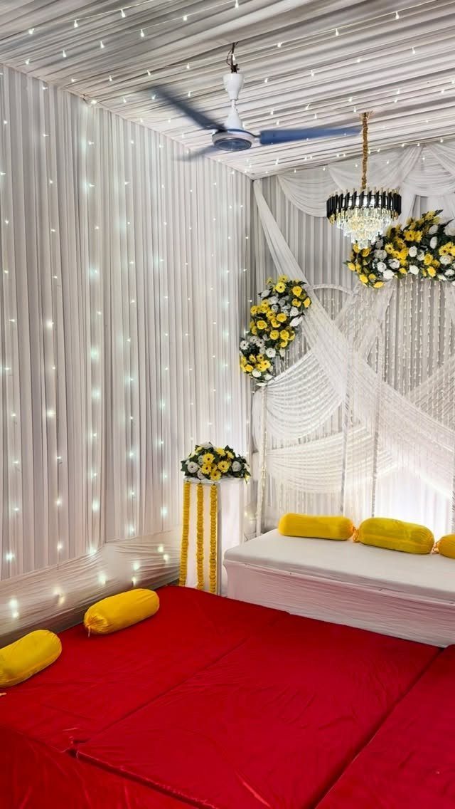 White draped event space with red flooring, yellow pillows, and yellow floral arrangements.