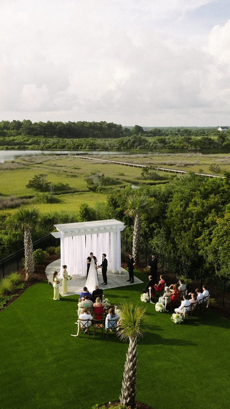 Wedding ceremony under a white pergola overlooking a scenic coastal marsh landscape