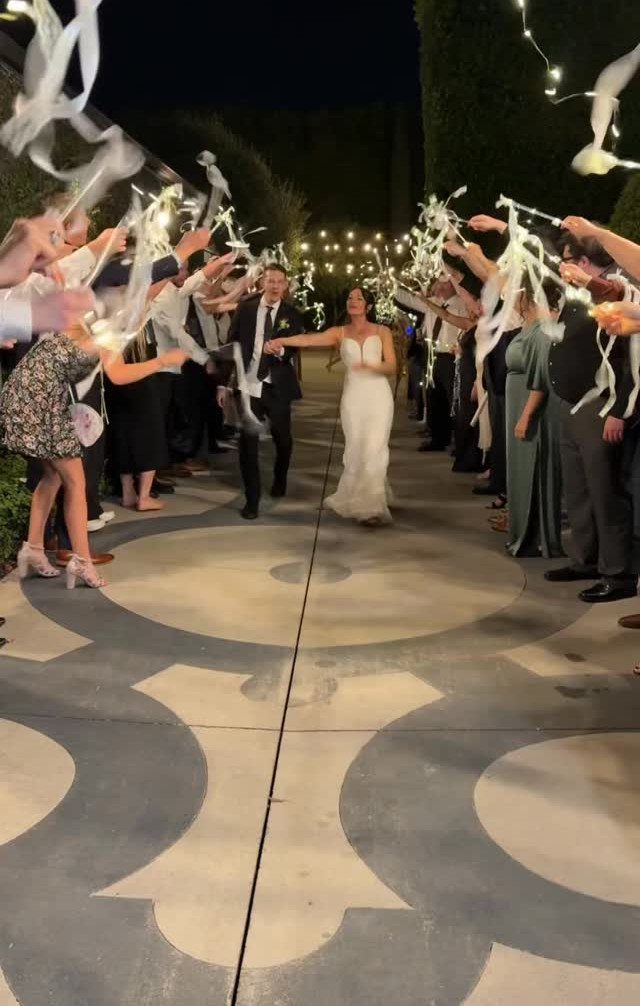 Bride and groom walking through a ribbon archway created by wedding guests at night