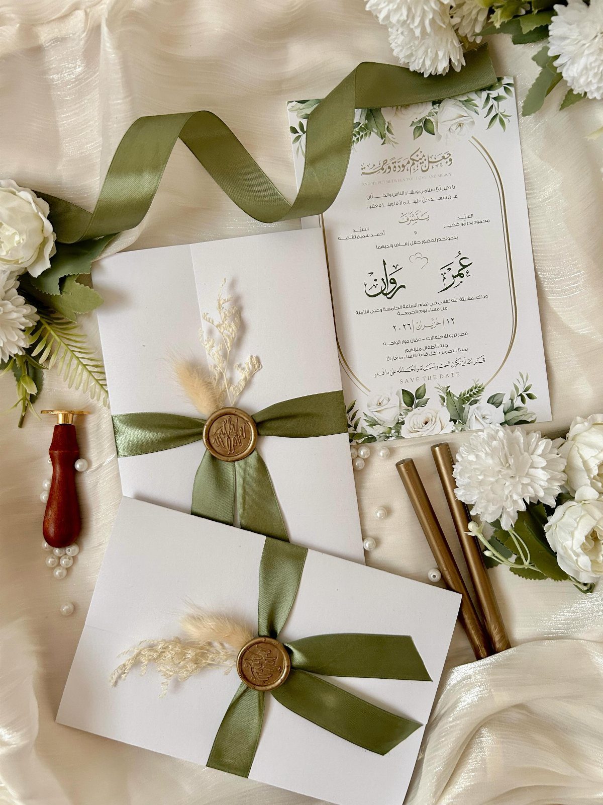 Sage green ribbons and gold wax seals on white wedding invitation stationery.