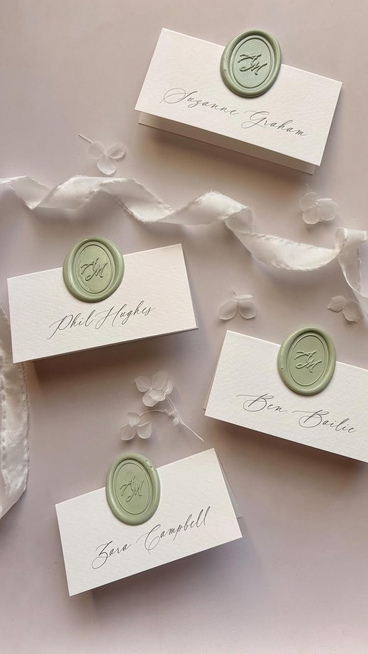 White place cards with sage green wax seals and cursive names on light background
