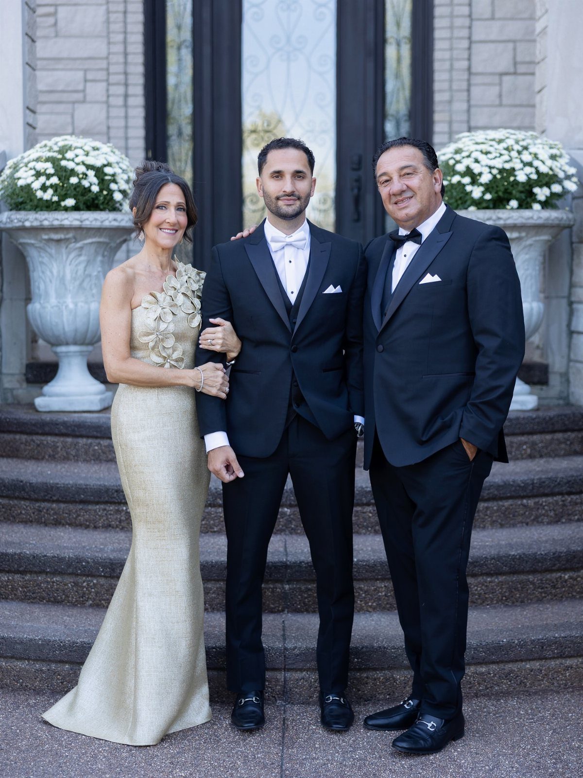Three formally dressed adults posing for a portrait on stone steps outdoors.