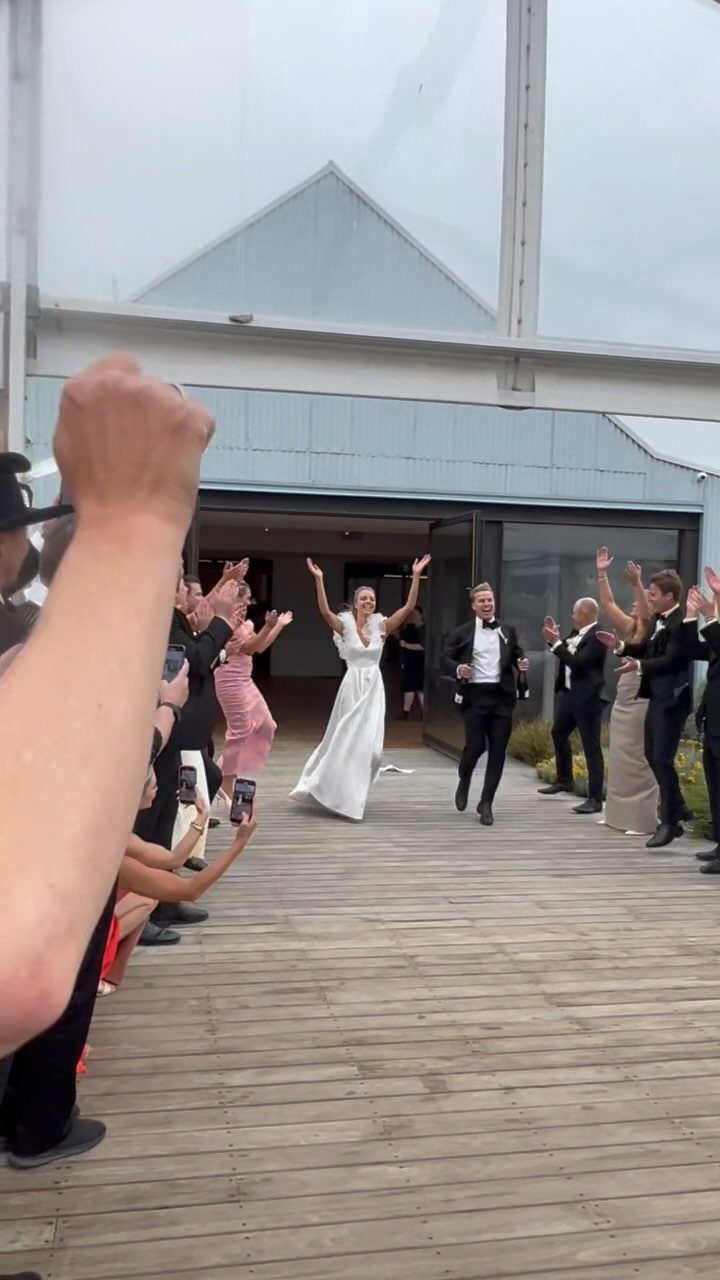 Bride and groom entering their wedding reception while guests cheer on a wooden deck