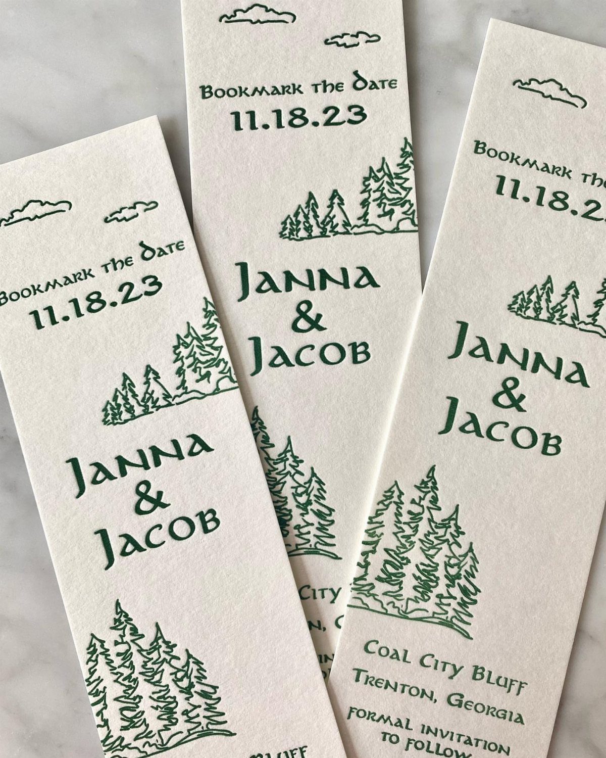 Three white cardstock bookmarks with green pine tree illustrations and wedding date text.