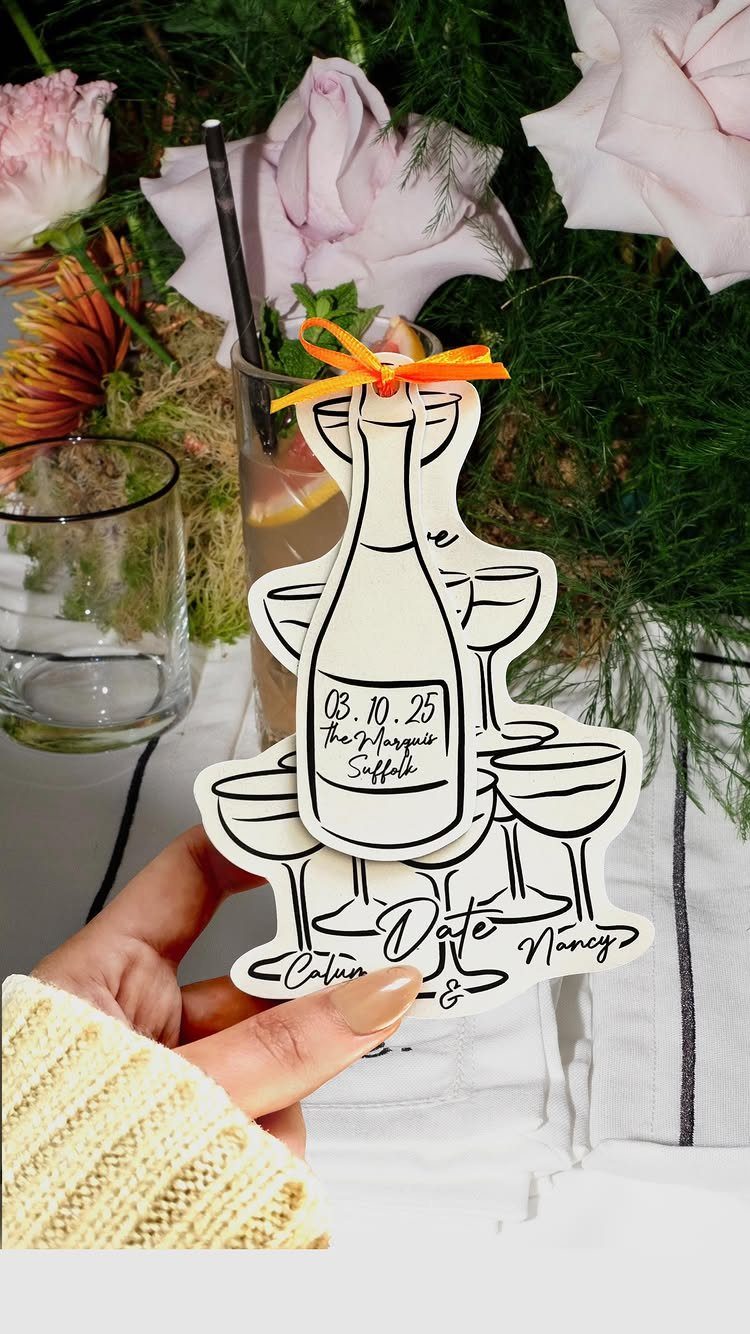 White die-cut save the date card shaped like champagne bottle and glasses.