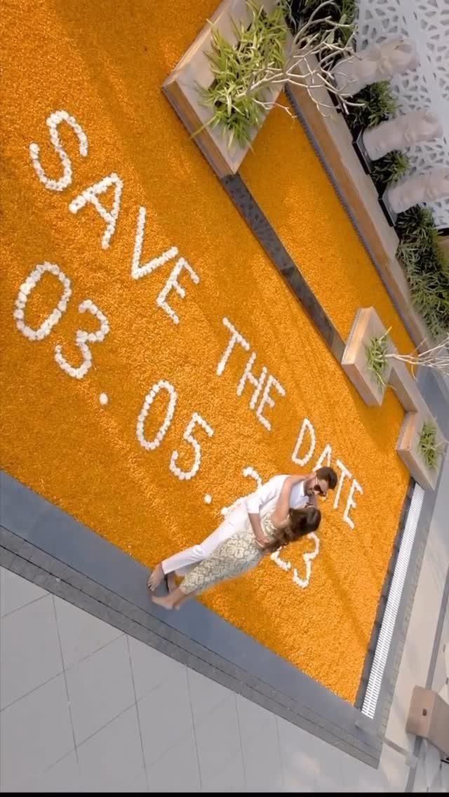 Couple embracing on orange ground with save the date written in white petals