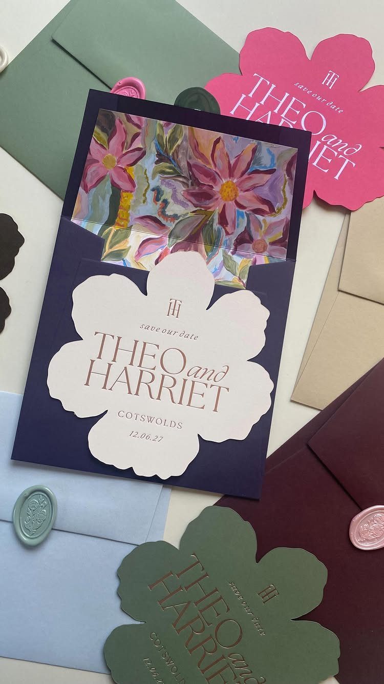 Floral-shaped save the date cards and envelopes in various colors with gold lettering.