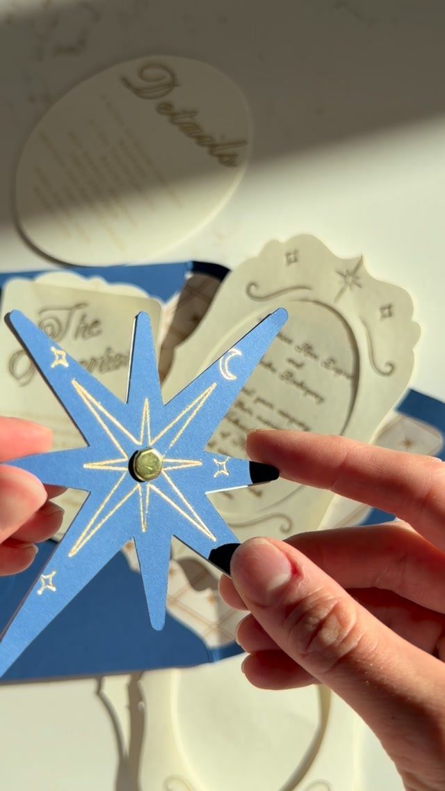 Blue star-shaped card with gold foil accents held by two hands over stationery.