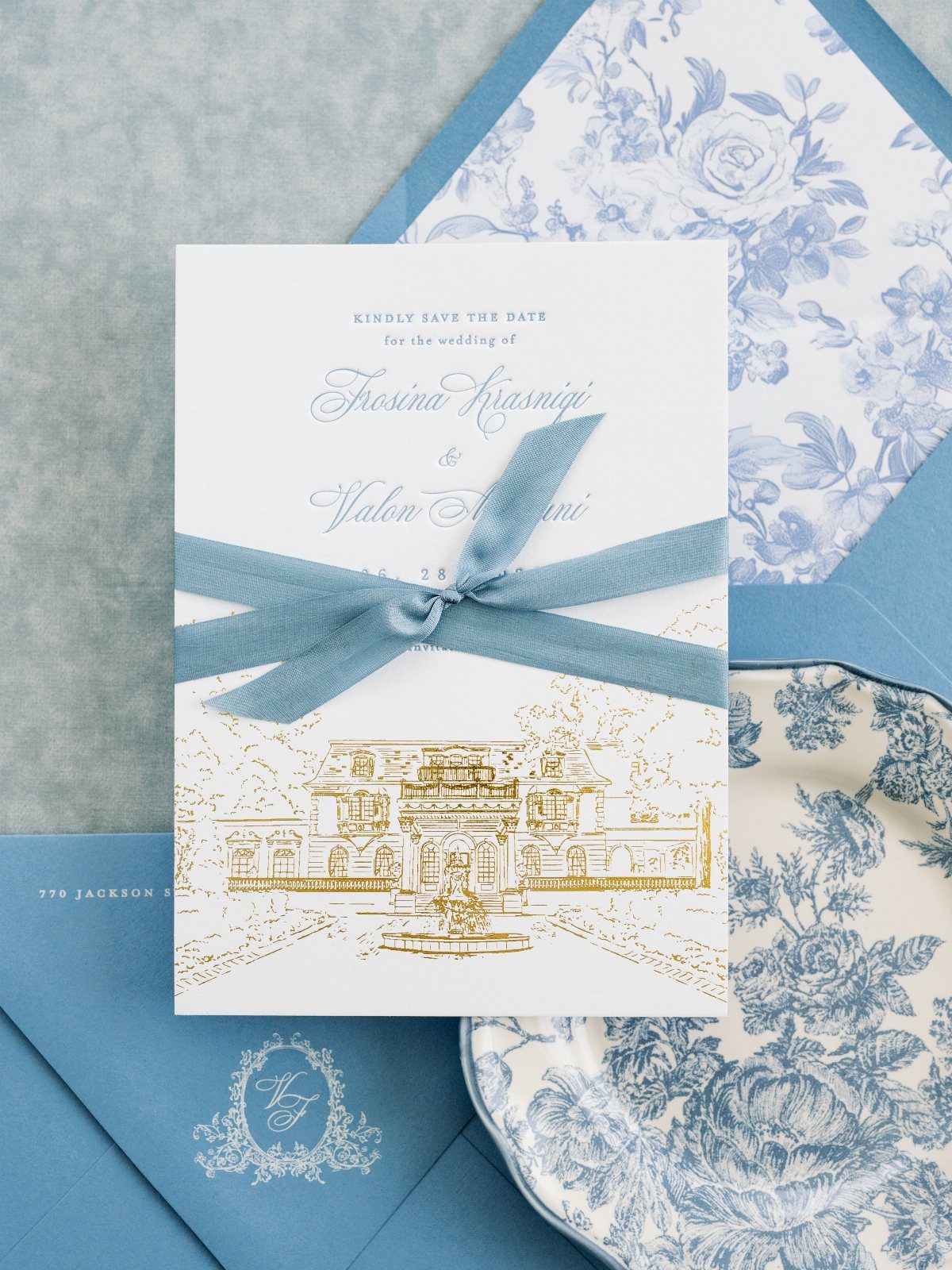Save the date card with blue script and gold illustration tied with blue ribbon.