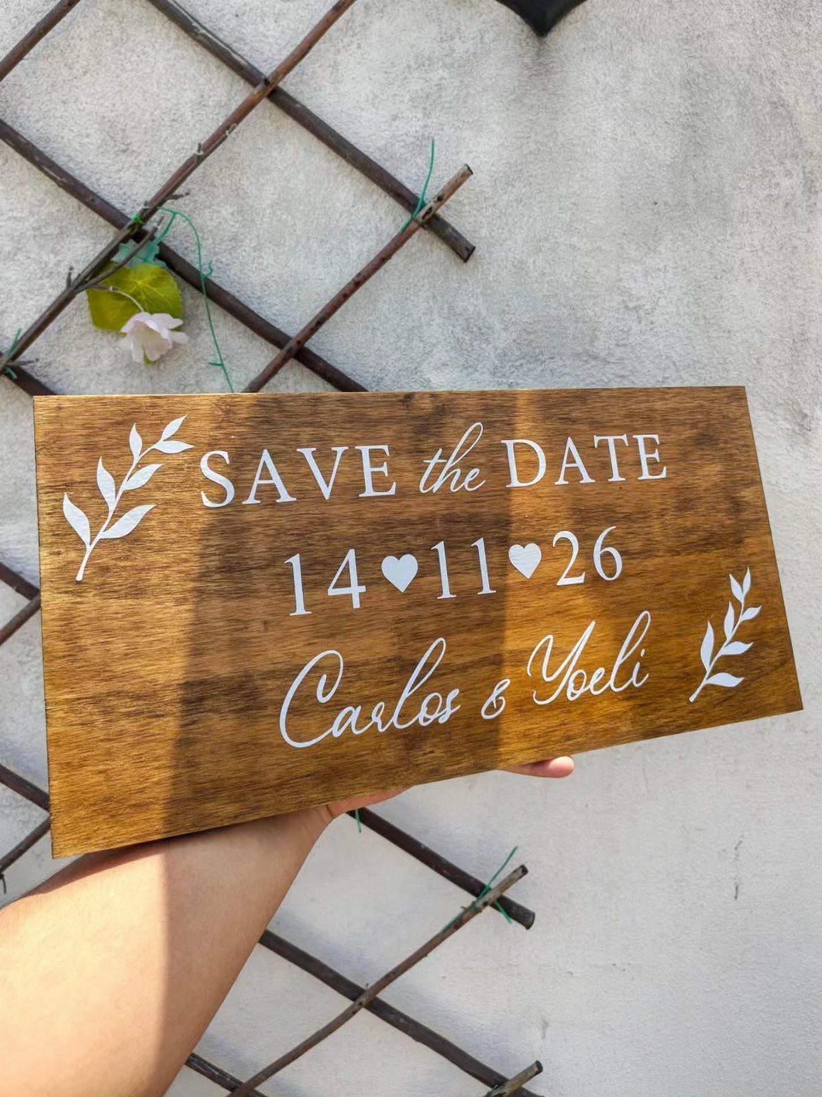 Wooden save the date plaque with white engraved text and leaf illustrations.