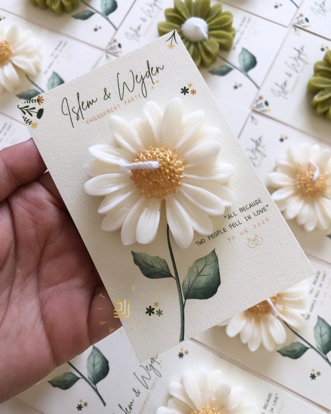 Daisy-shaped white candles attached to elegant engagement party announcement cards with floral designs.