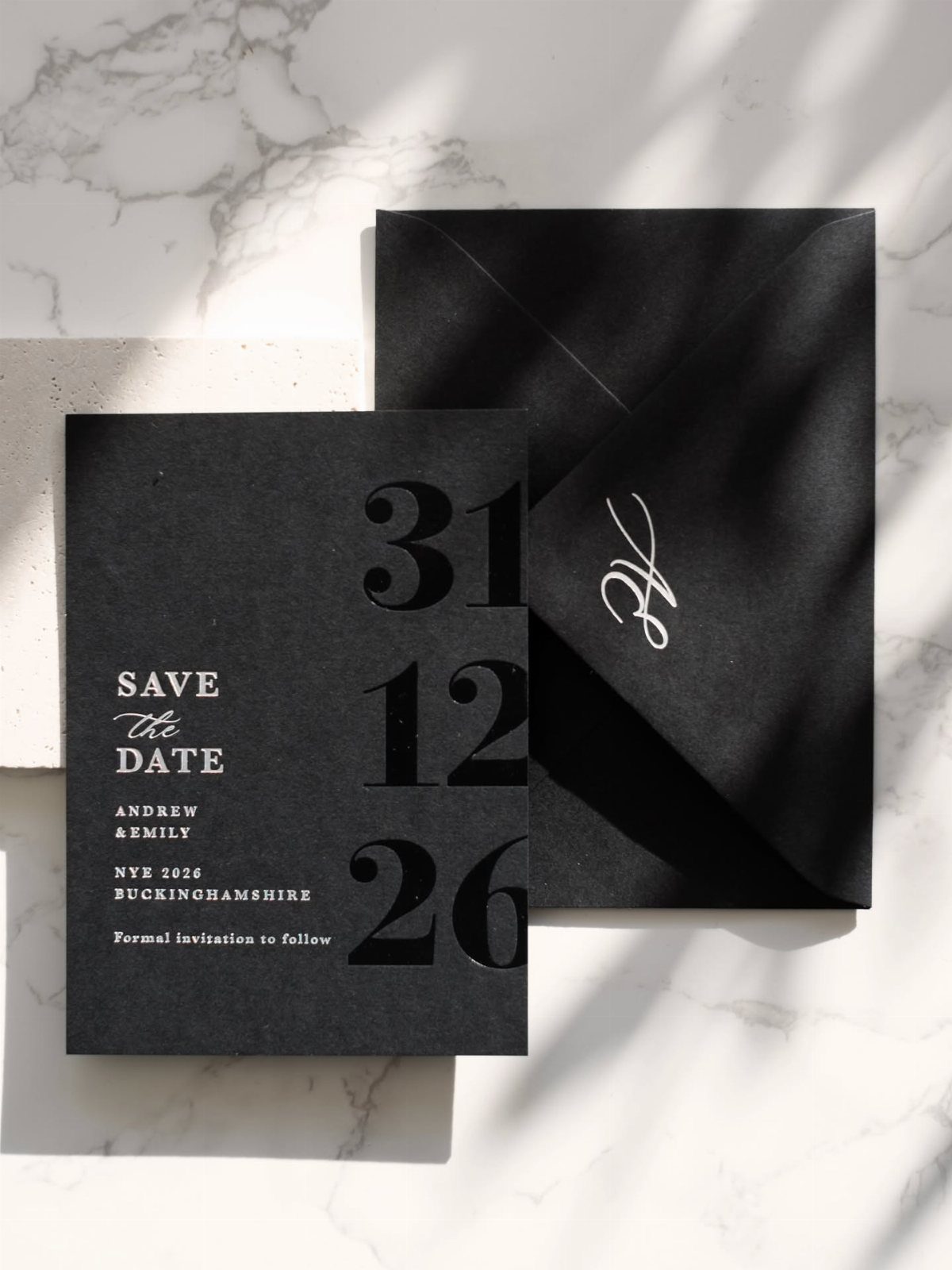 Black save the date card and envelope with white typography on marble background