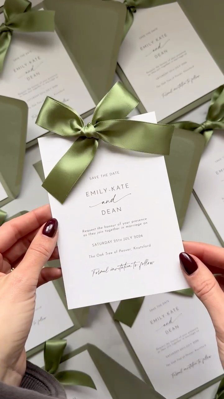 White save the date card with a green satin bow held by hands.