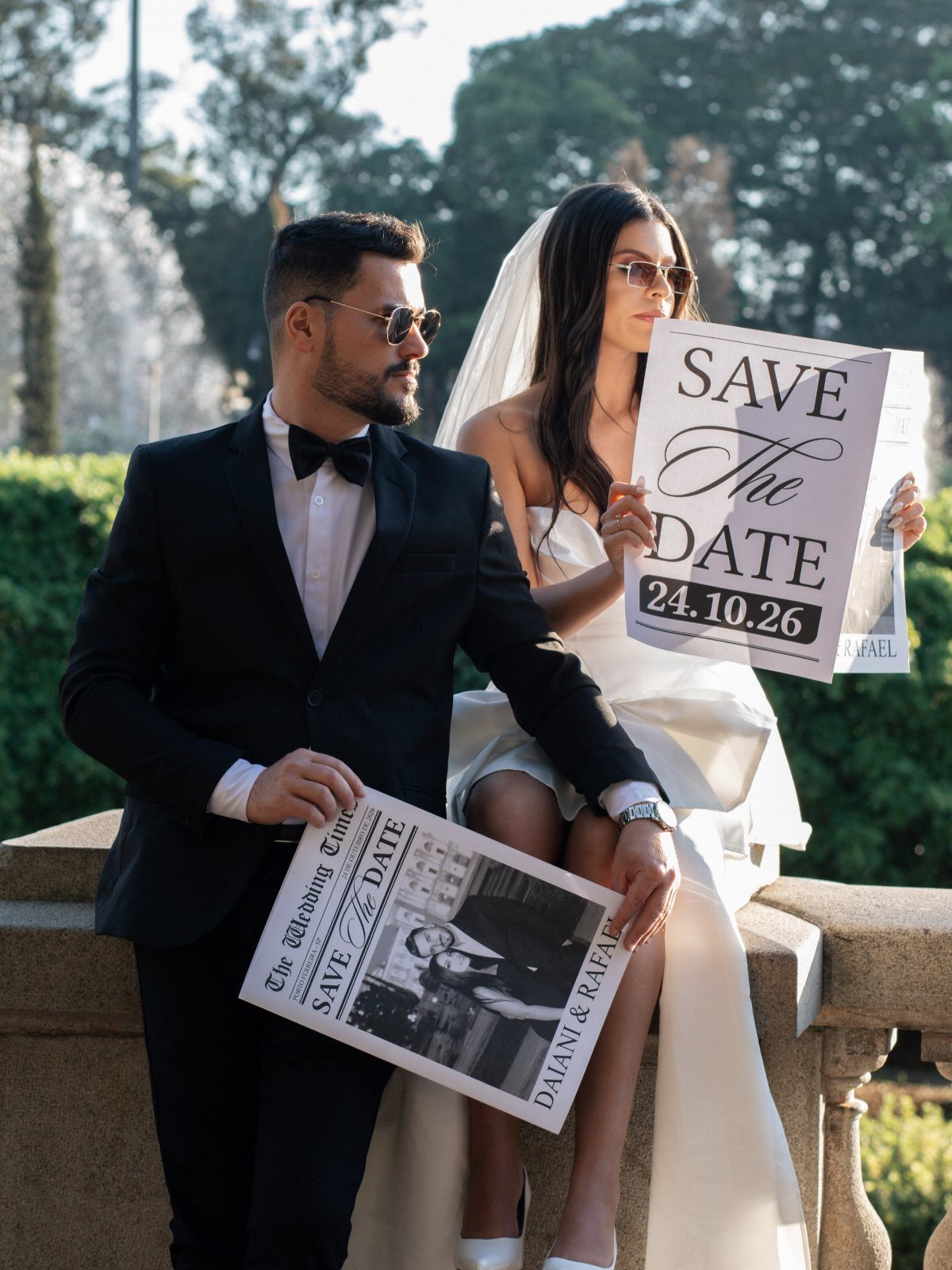 Bride and groom in formal attire holding save the date signs outdoors.