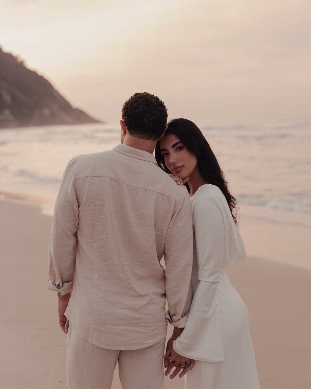 Couple posing on a beach at sunset with woman leaning on man's shoulder