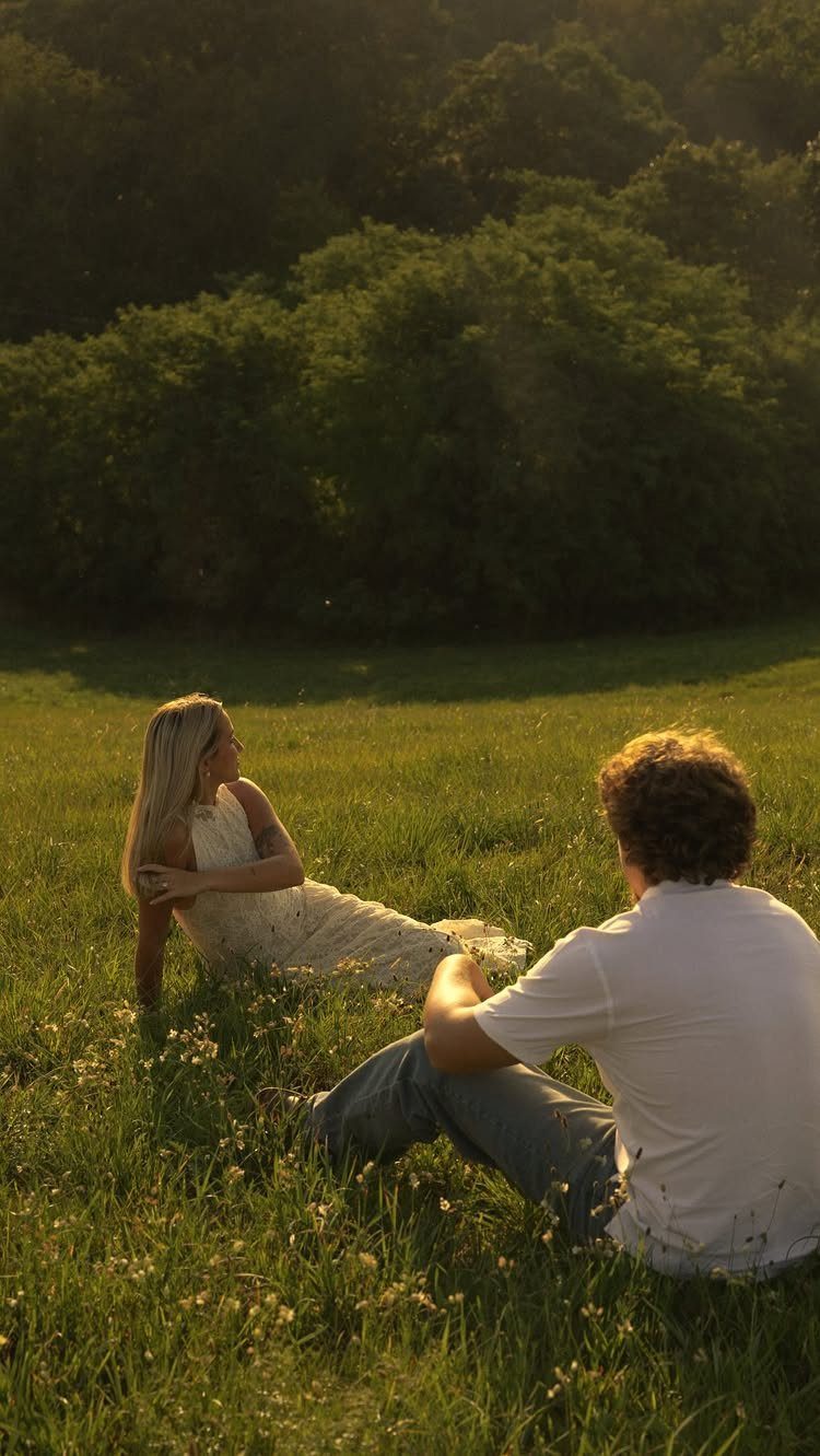 Couple sitting in a sunlit grassy field with trees in the background.