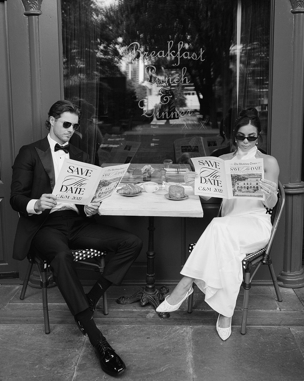 Couple in retro formal attire sitting at a cafe reading save the date newspapers.