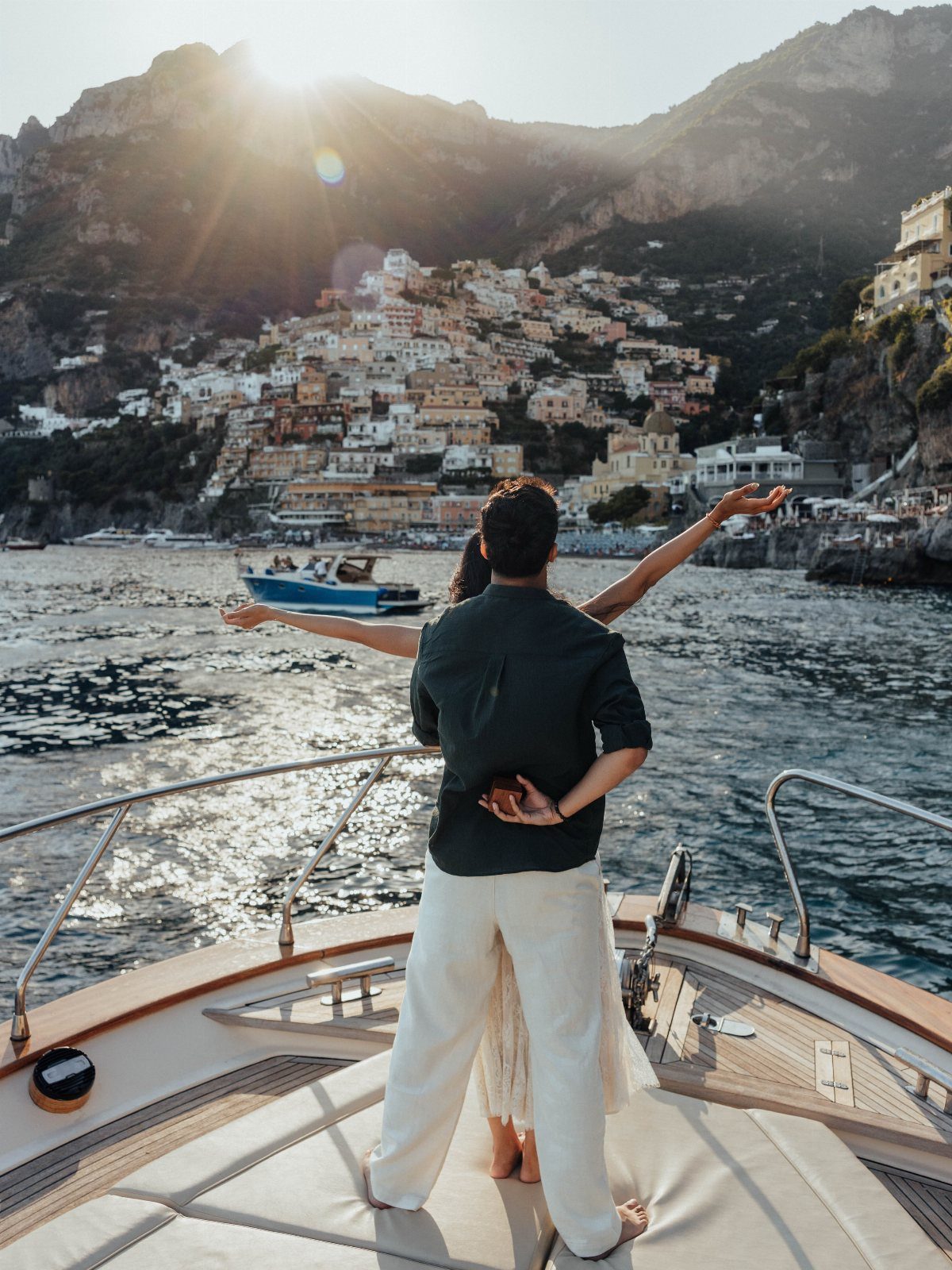 Couple on a boat deck overlooking a scenic coastal town and mountains.