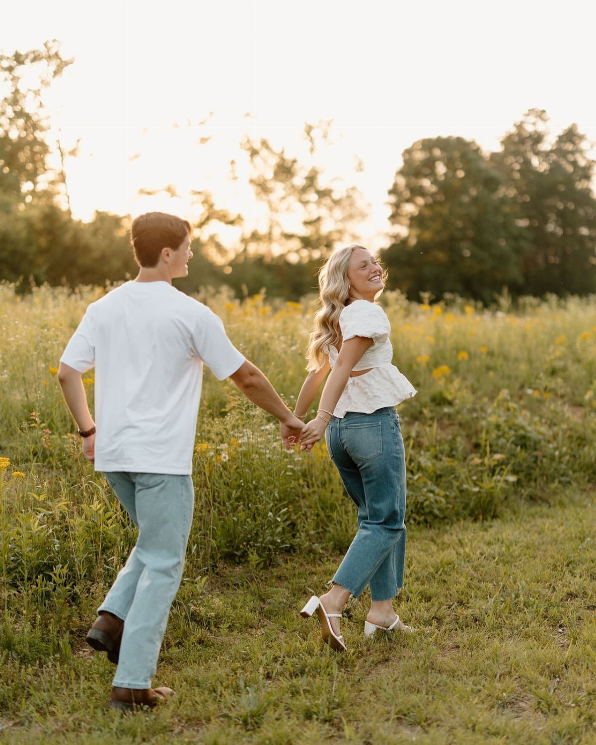Couple holding hands while walking through a sunny field of yellow wildflowers.