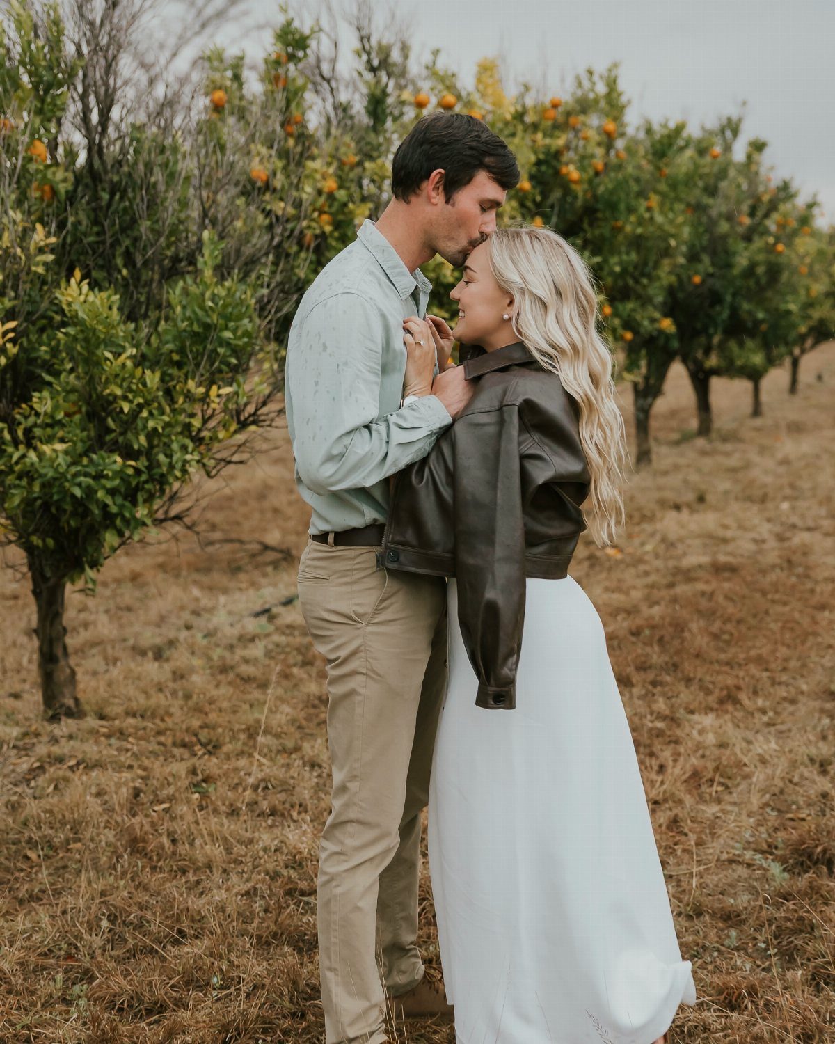 Couple embracing in an orange grove with trees and fruit in the background