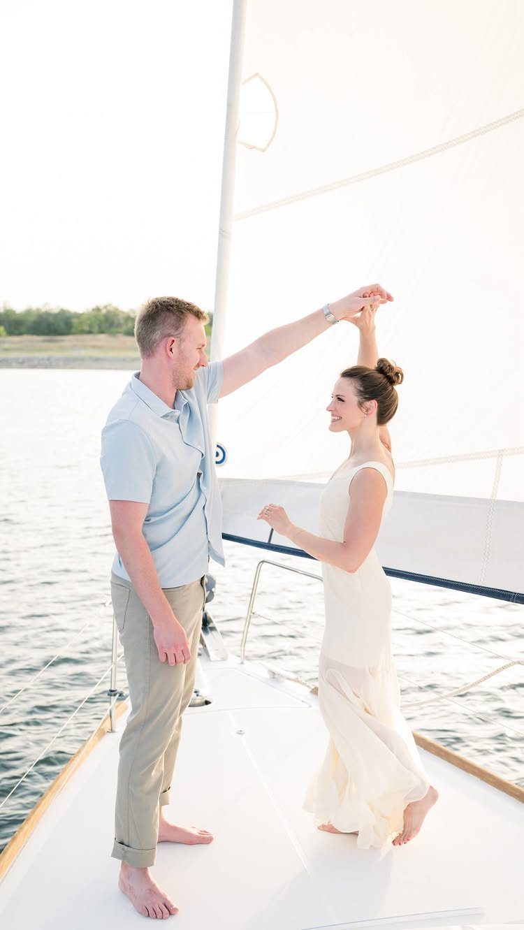 Couple dancing on a sailboat deck with a white sail and water background