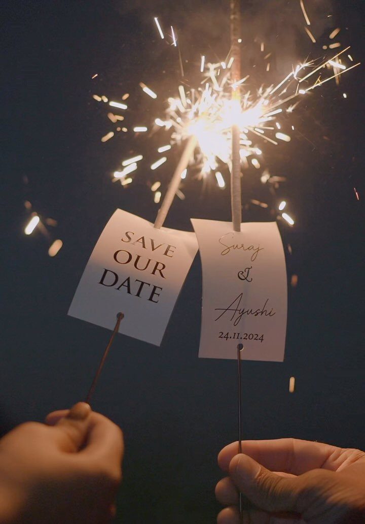 Lit sparklers held by two people with save the date cards attached.