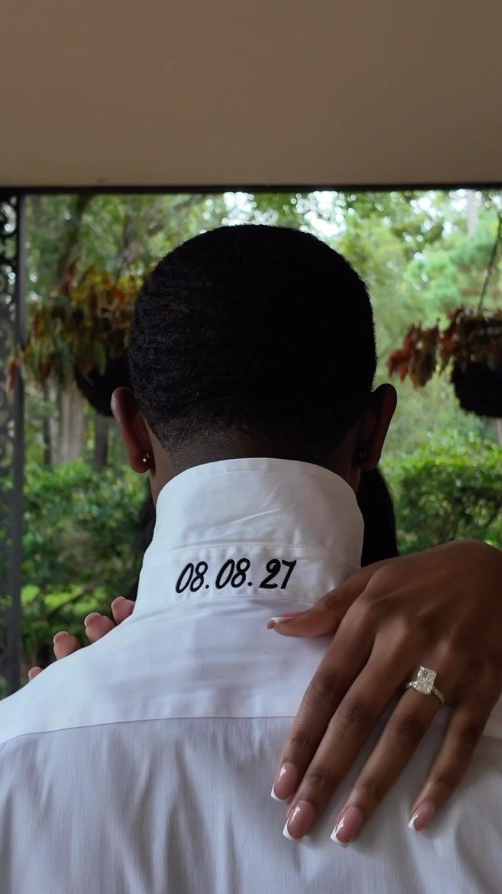 Embroidered wedding date on a white shirt collar with a hand wearing a ring.
