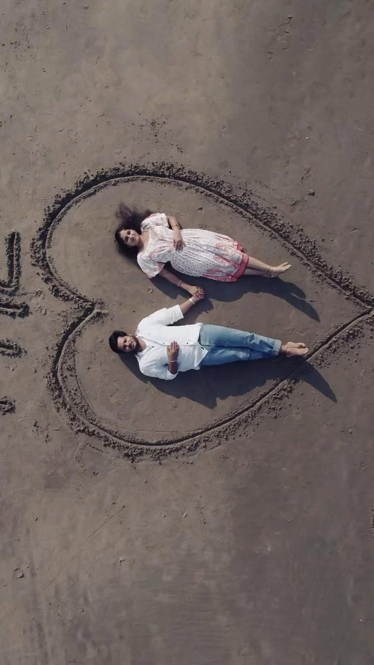 Couple lying inside a large heart drawn in the sand on a beach.