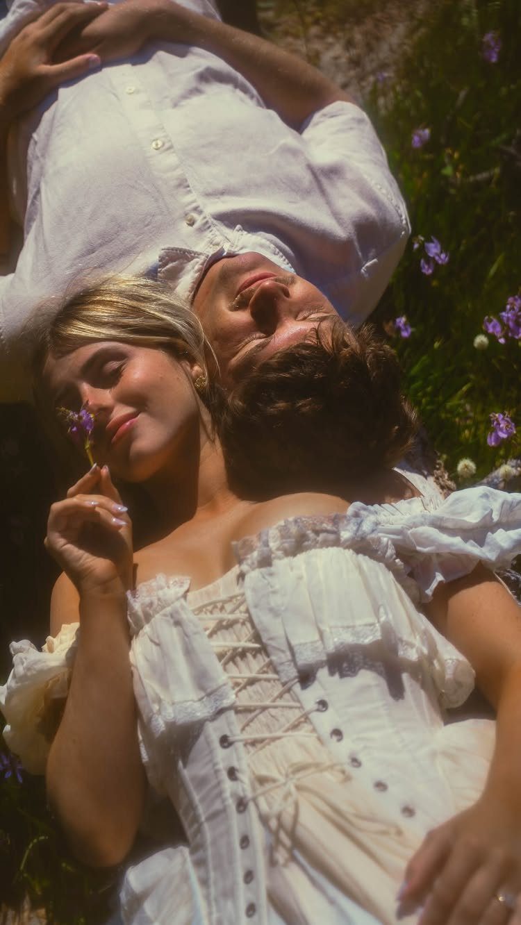 Couple lying head-to-head in a sunny field wearing white vintage clothing.